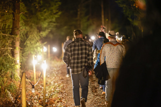 Folk går på opplyst sti i skogen om kvelden