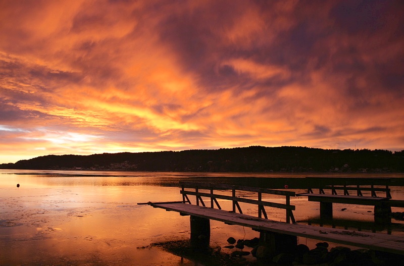 Oransje solnedgang over vann og brygge