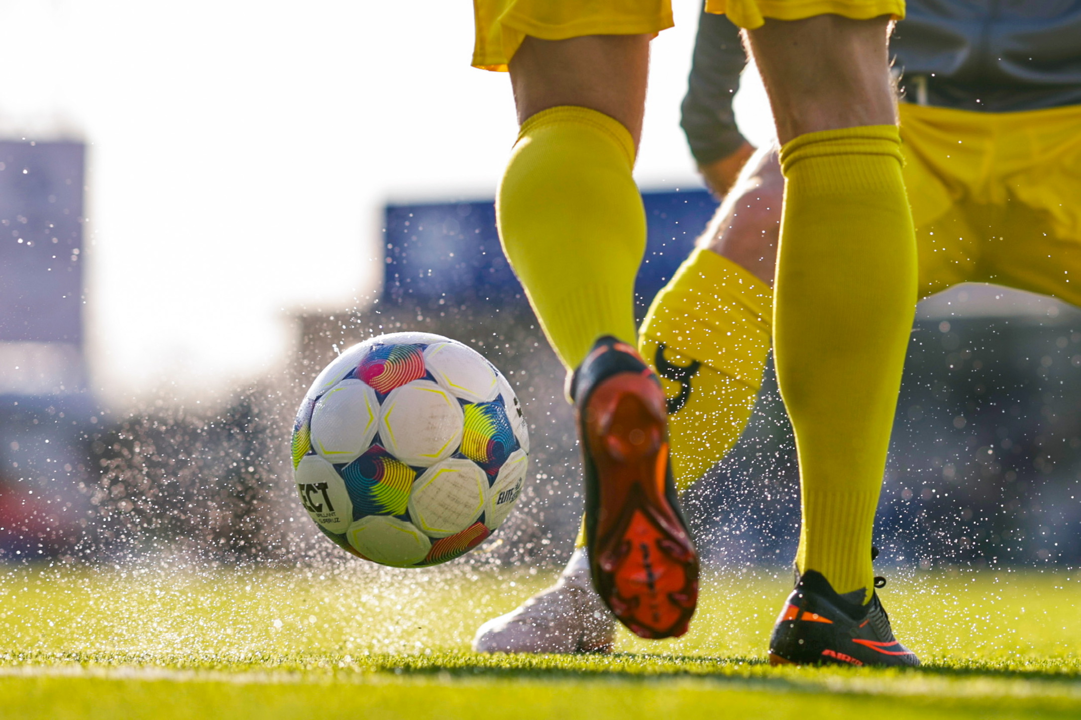 Fotball og støv/vannsprut ved spillere i gule sokker