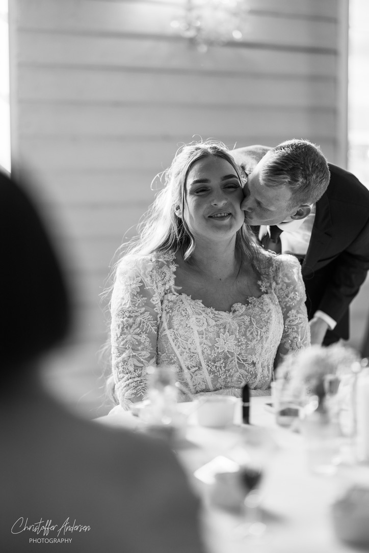 Brud får kyss på kinnet under bryllupsmiddag