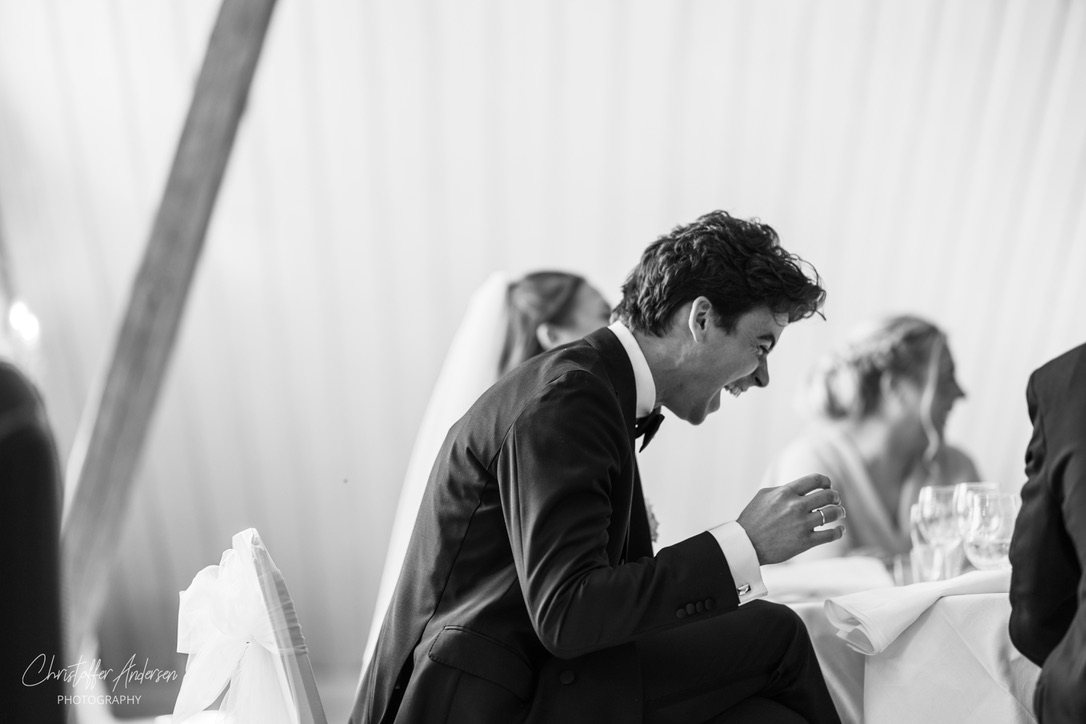 Brudgom ler under bryllupsmiddag i sort-hvitt
